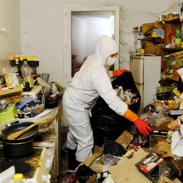 Intervenant en tenue de protection préparant le nettoyage d'un logement encombré après un décès